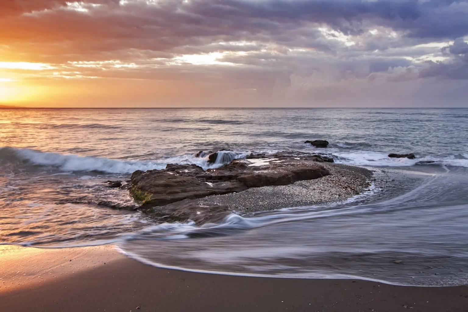 A serene beach scene with soft waves lapping at golden sand under a clear blue sky.